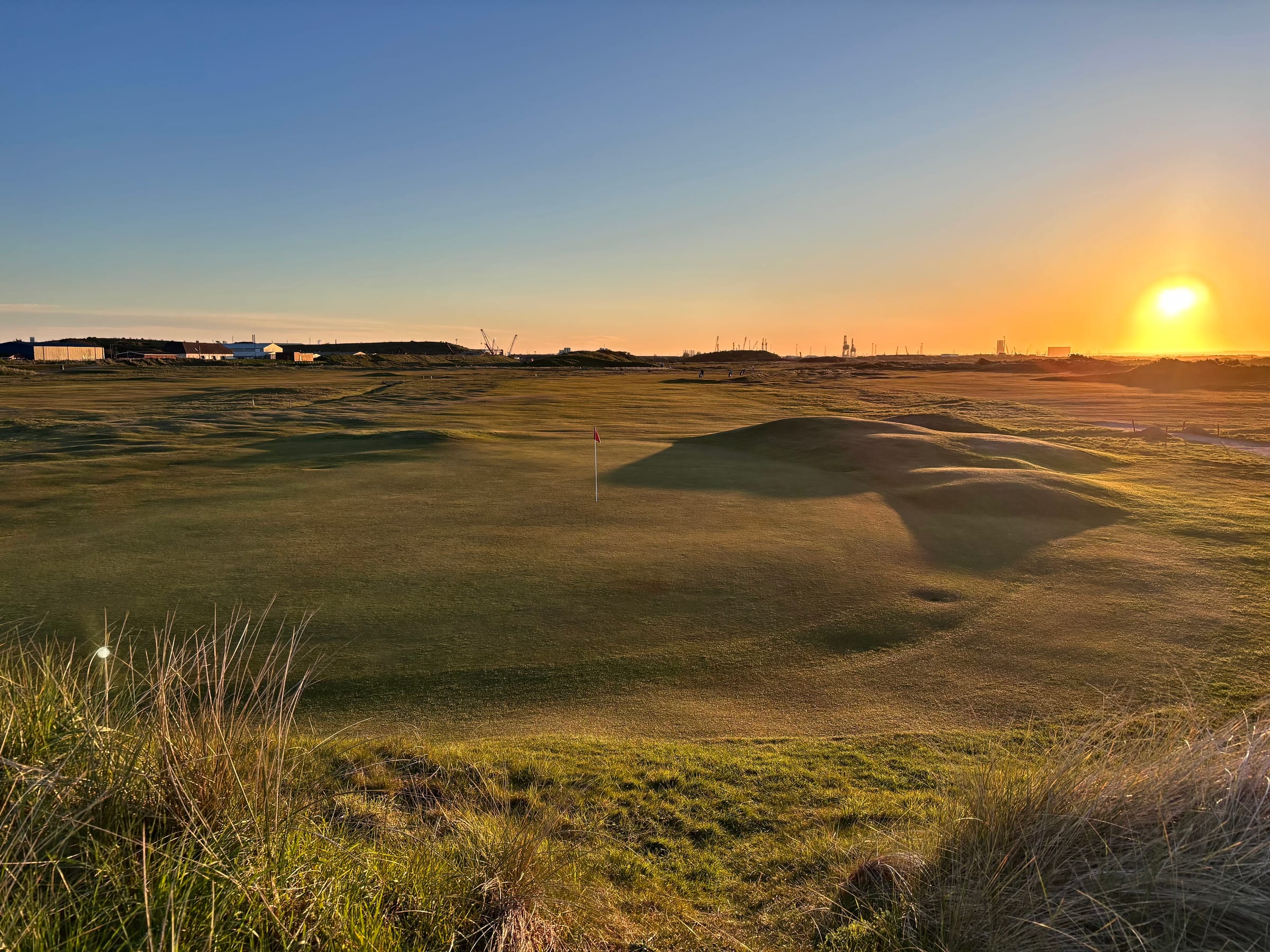 A green on Cleveland Golf Club's links course at sunset, with dunes and the flag lit by golden-hour light