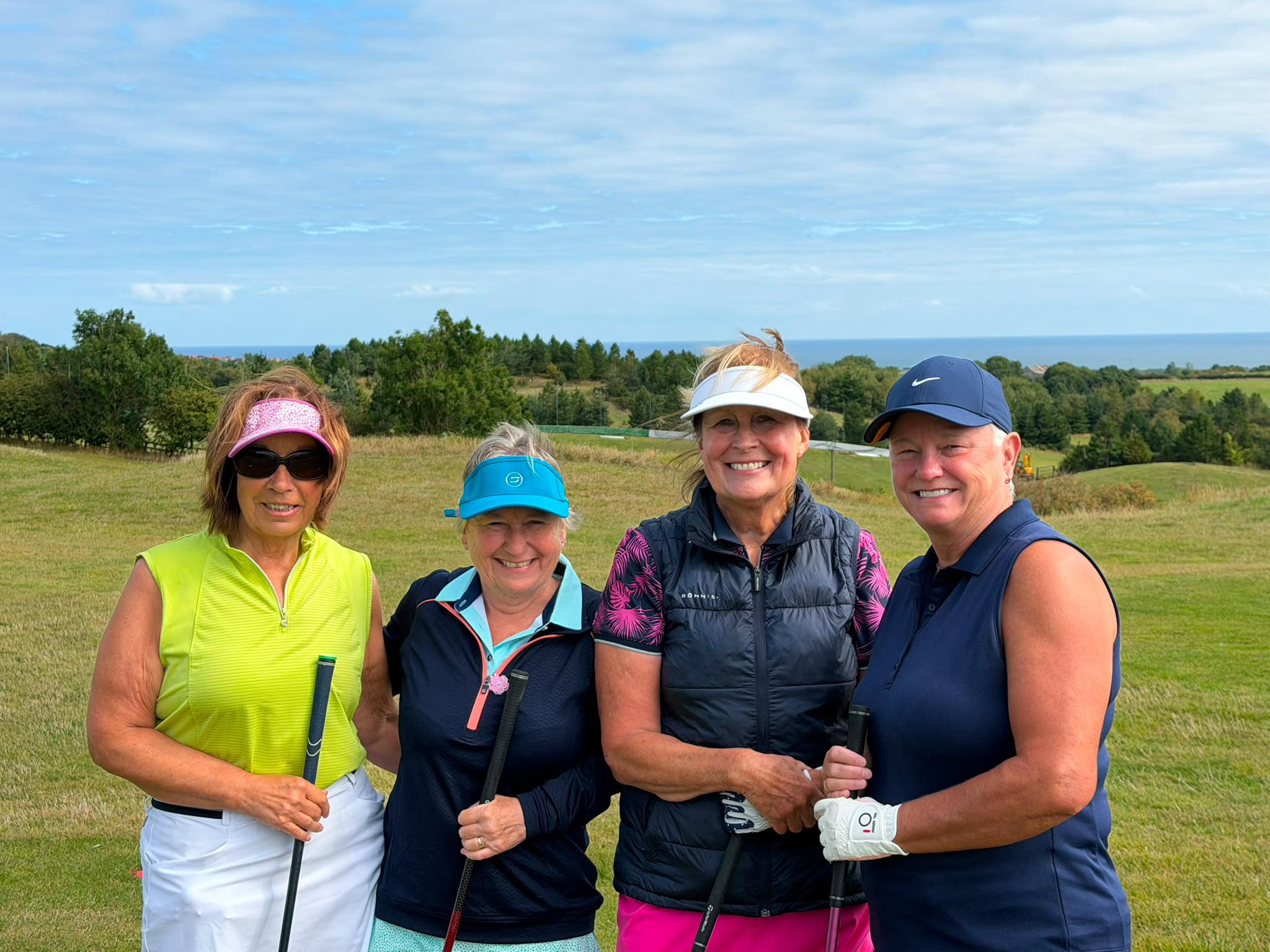 Four Cleveland Golf Club lady members smiling together on the course before a round, with the coastline visible in the distance