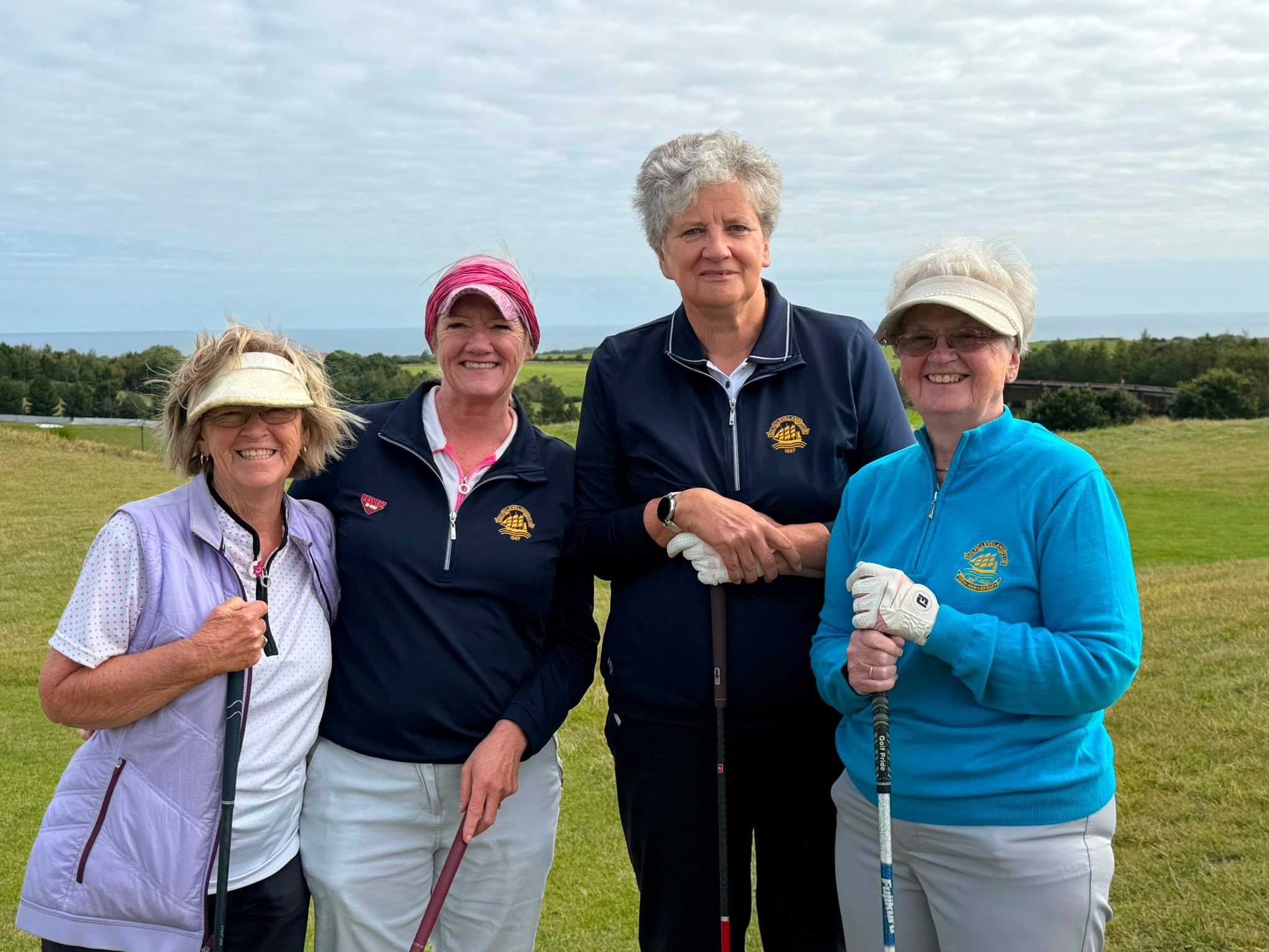 Four Cleveland Golf Club lady members in club-crested tops pausing together on the course