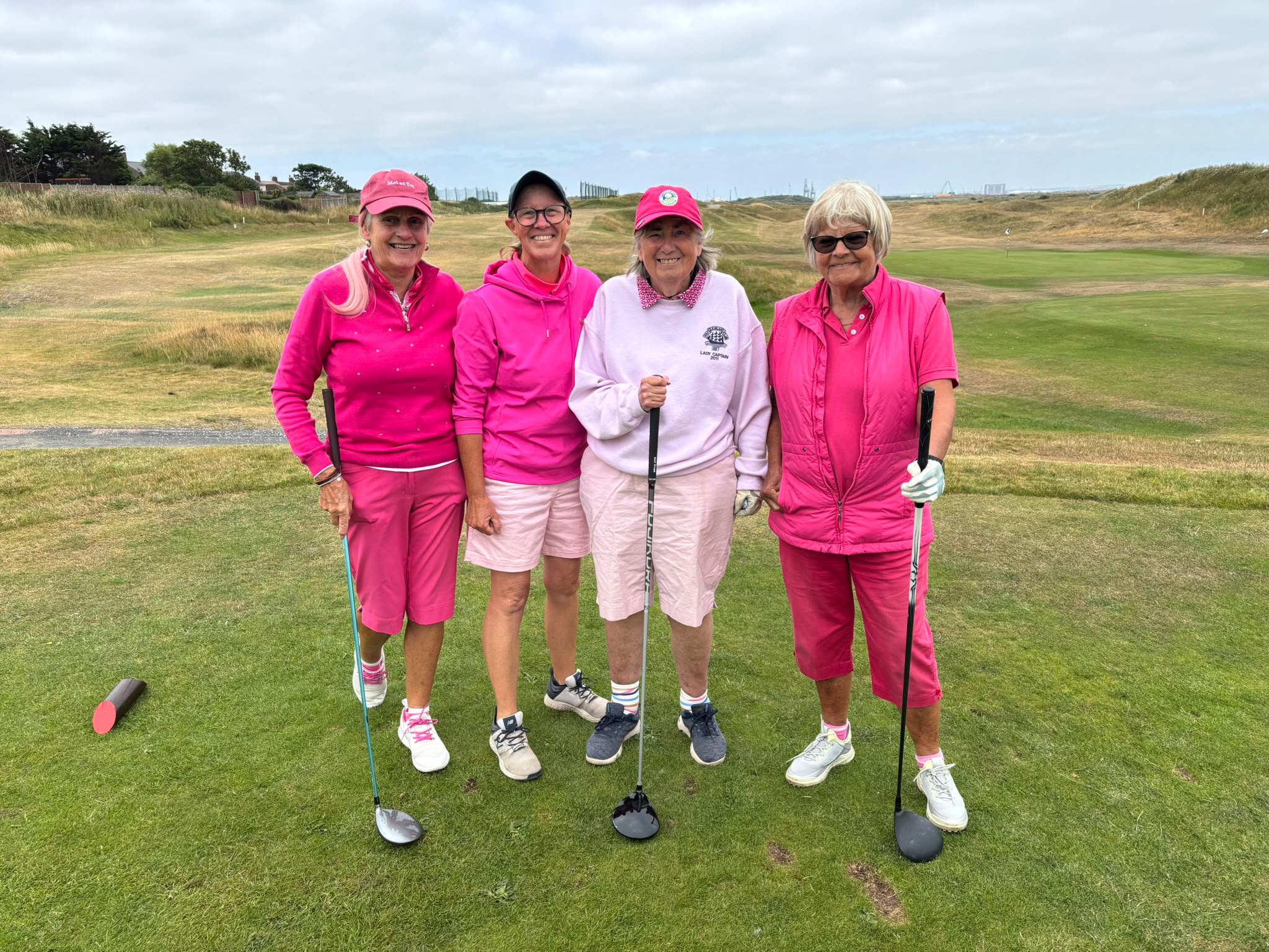 Four Cleveland Golf Club lady members in pink outfits on the links, with a green and flag visible behind them