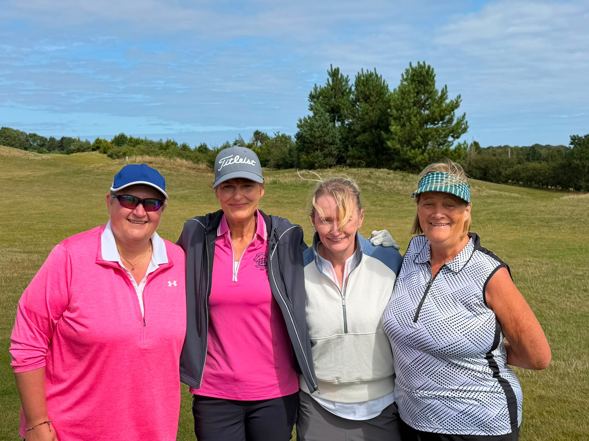 Four Cleveland Golf Club lady members smiling together on the fairway, with pine trees and rolling hills behind them