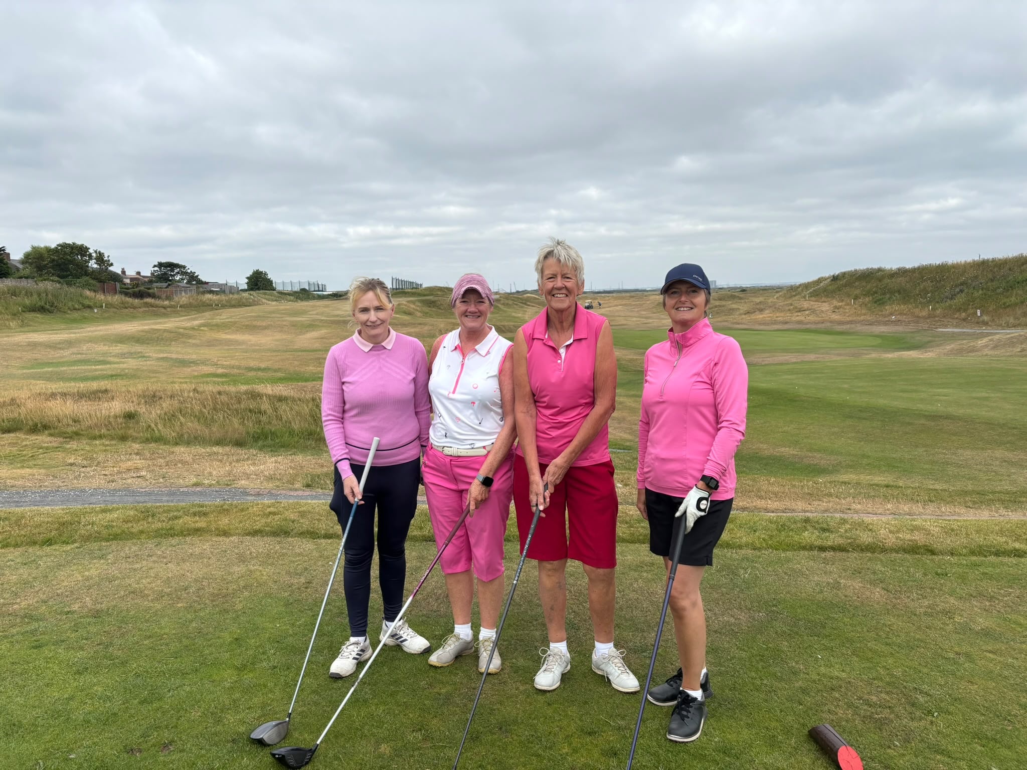 Four Cleveland Golf Club lady members dressed in pink on the tee, with a long fairway and dunes stretching into the distance