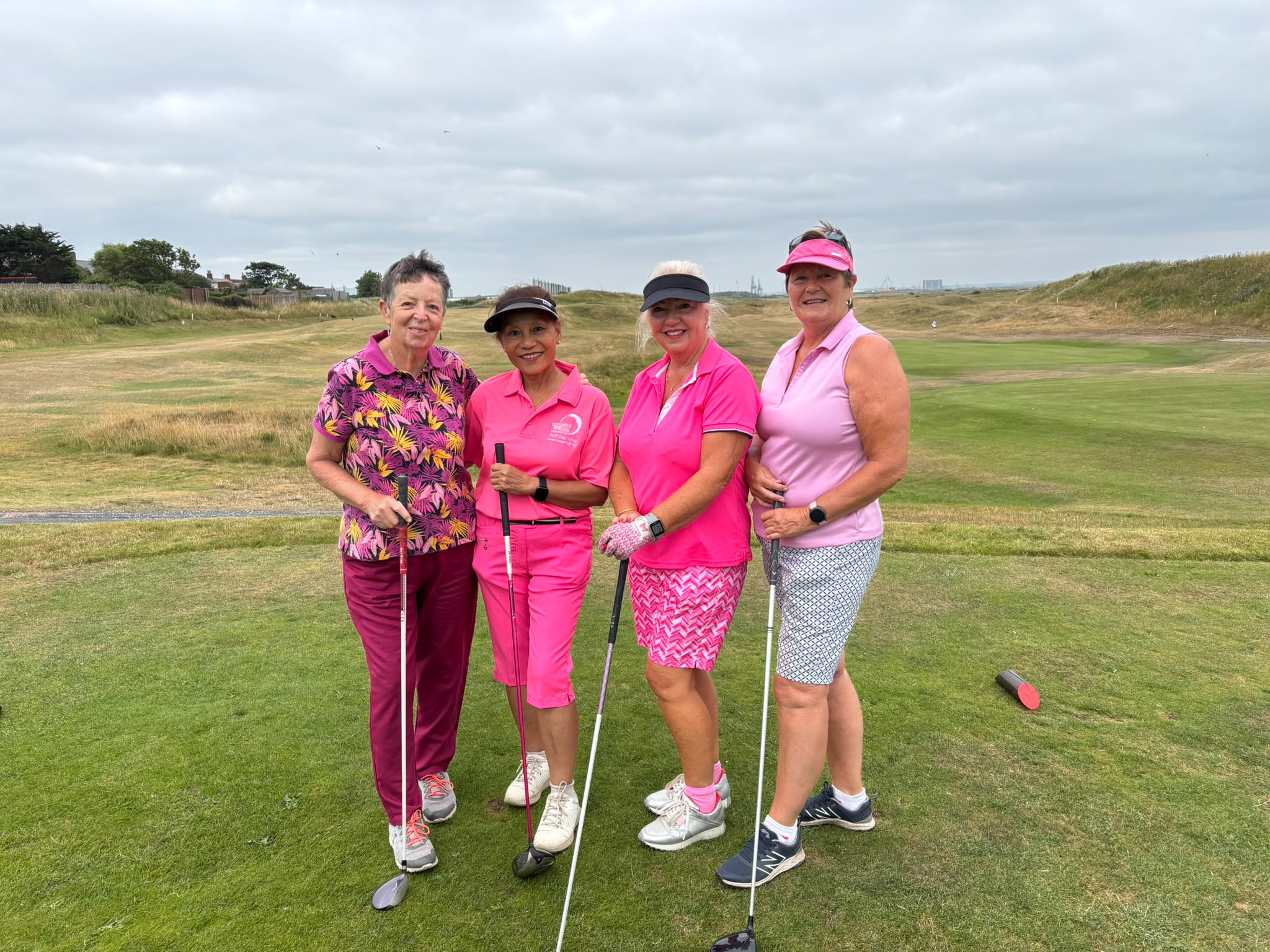 Four Cleveland Golf Club lady members dressed in pink, standing together near the green with the flag and coastline visible behind them